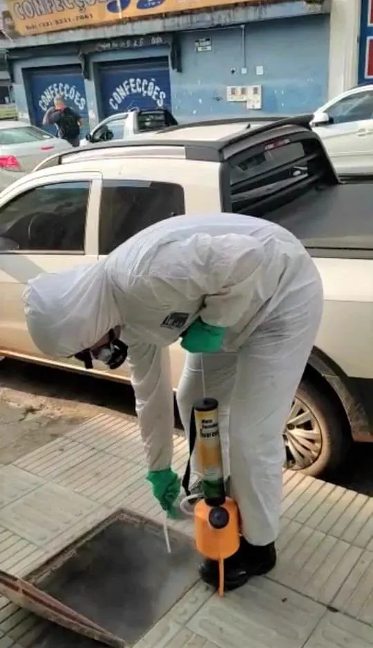 Técnico da Praban com EPI completo aplicando produto em bueiro na calçada
