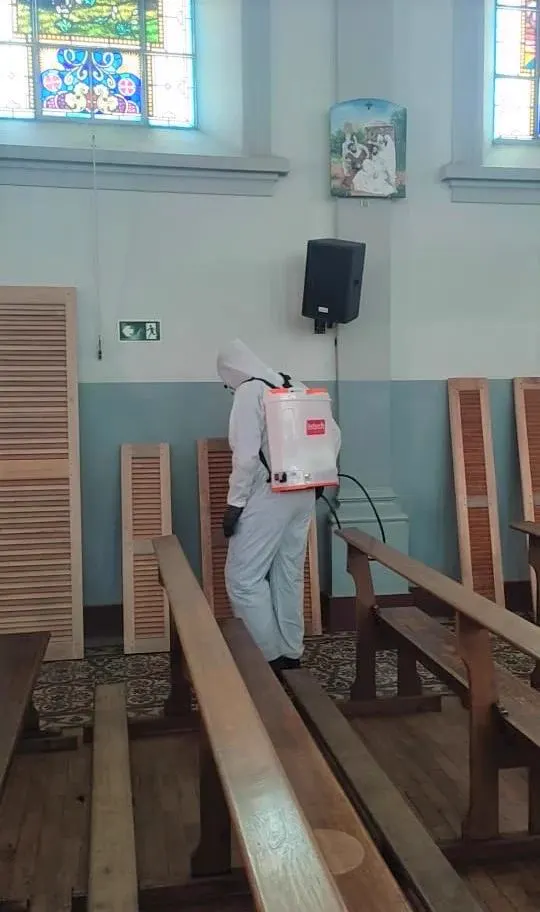 Técnico da Praban de macacão fazendo aplicação entre os bancos de uma igreja