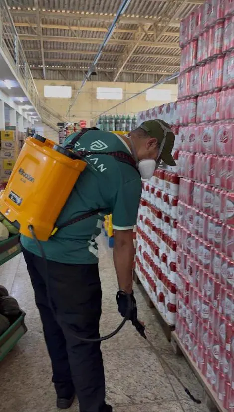 Técnico uniformizado da Praban com pulverizador costal nos corredores de um supermercado